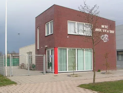 Het clubhuis van WTC Houten ’80: een bakstenen gebouw met grote ramen en een rode pilaar bij de ingang, met op de gevel de naam van de club en het logo