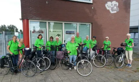 Recreanten in het groene clubtenue met hun fietsen voor het clubhuis