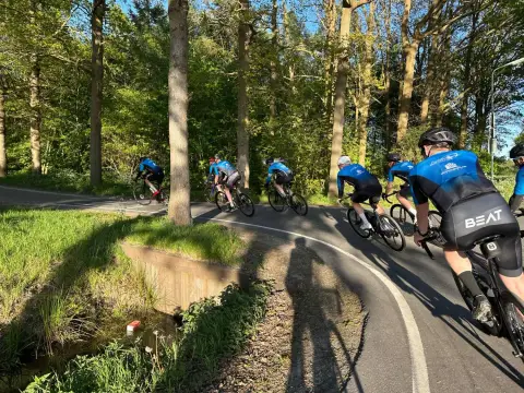 Toerleden op de racefiets door een bocht in het bos, in de avondzon