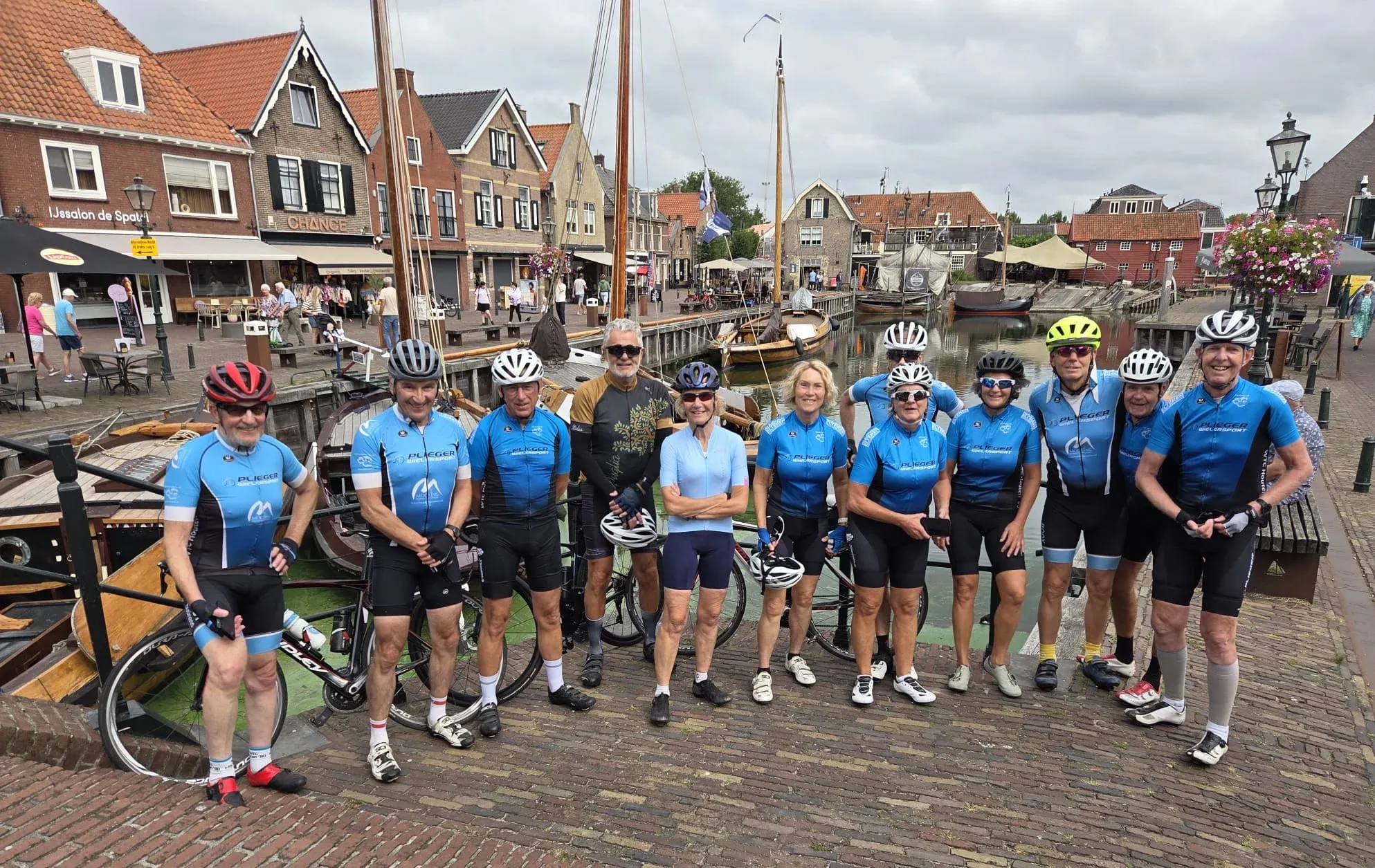 Een lachende groep toerleden in het blauwe clubtenue aan de haven van Spakenburg, met houten zeilschepen erachter
