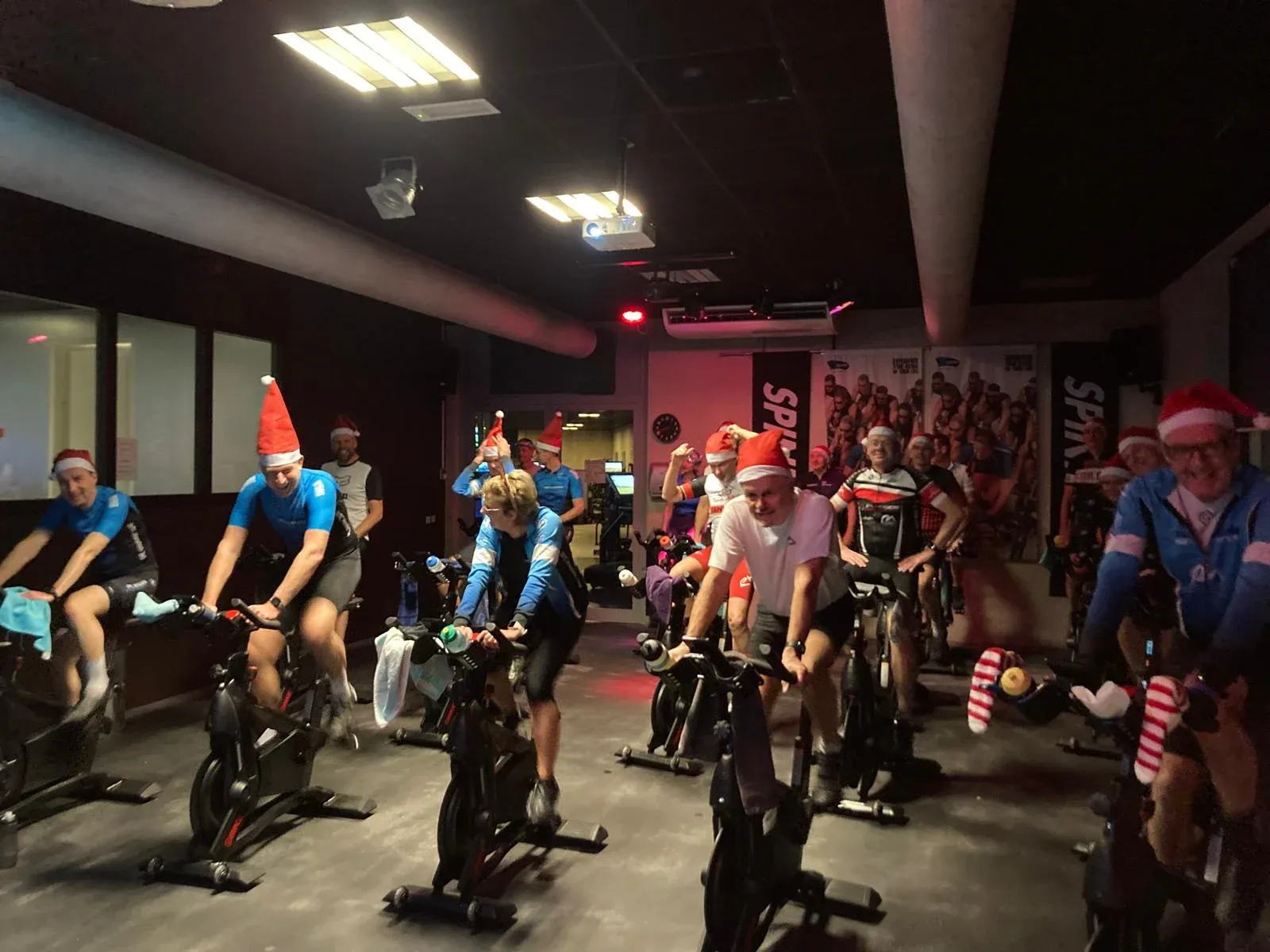 Clubleden met kerstmutsen op spinningfietsen tijdens een spinningles in de sportschool