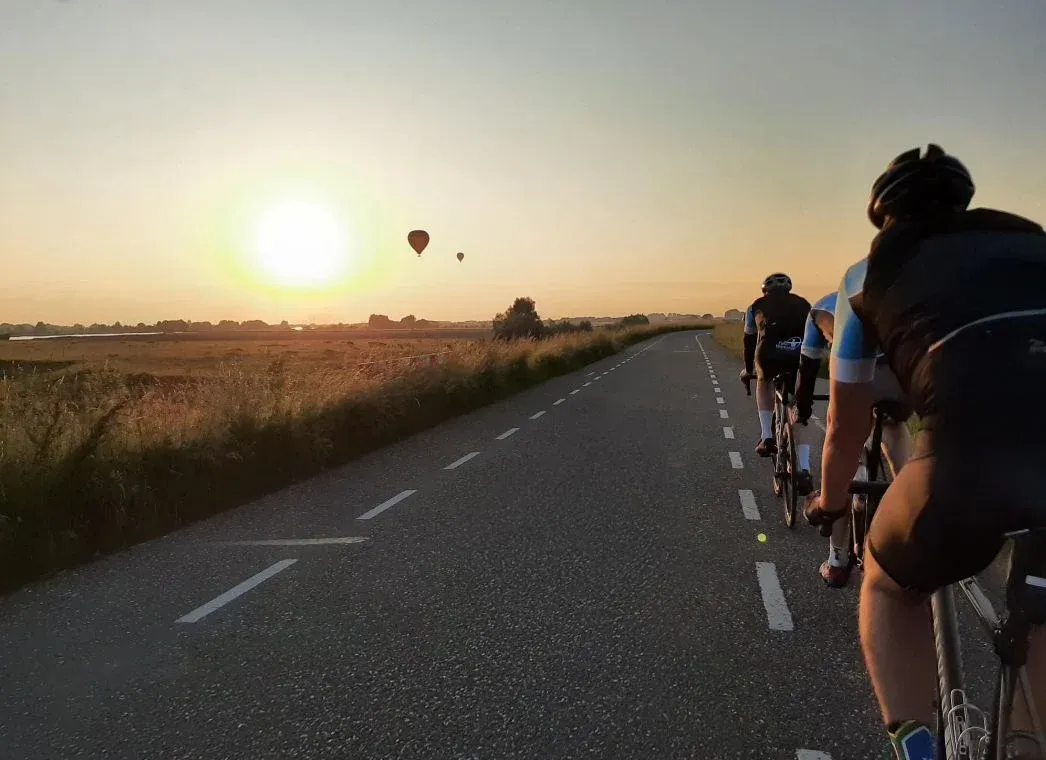 Toerleden van achteren gezien op een polderweg bij zonsondergang, met twee luchtballonnen in de lucht